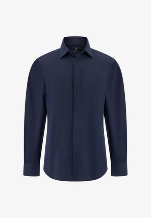 Tummansininen pitkähihaisella paidalla, jossa on napitettavat kaulukset, edessä napit ja sileä tekstuuri. Ominaisuuksiin kuuluu muotoiltu istuvuus ja rakenteelliset olkapäät.