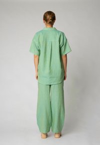 Completo in lino verde, leggero, con una camicia dalla vestibilità ampia e pantaloni a gamba larga. Il tessuto presenta un motivo testurizzato e sottile.