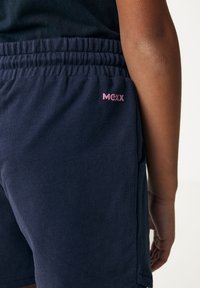 Shorts de algodón azul marino con cintura elástica, que cuentan con un logo rosa de "Mexx" en el lado derecho y bolsillos laterales. Textura suave.