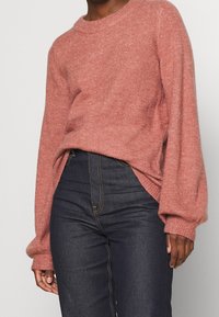 Lichtroze, zachte gebreide trui met lange, ballonvormige mouwen en een geribde halslijn, gecombineerd met hoge taille, donkerdenim jeans.