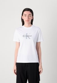 Camiseta de algodón blanca con un logo gris de Calvin Klein, escote redondo clásico, mangas cortas y un corte relajado.