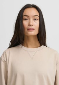 Beige pikendustega, pika varrukaga dressipluus ümar krae ning sellel on kaunis V-õmblusdetail kaeluses ja sile, pehme tekstuur.