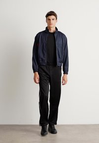 Ναυτικό αθλητικό μπουφάν με μολυβένιο γιακά, φερμουάρ μπροστά και ελαστικούς καρπούς, σε συνδυασμό με μαύρα παντελόνια που έχουν λευκές λωρίδες στο πλάι και μαύρα αθλητικά παπούτσια.