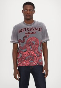 Grijs grafisch T-shirt met een rode illustratieve afbeelding van slangen en gezichten. Ronde hals, korte mouwen, relaxed fit, met gedrukte tekst.