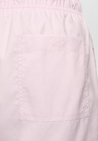 Shorts rose clair avec une taille élastique, dotés d'une poche latérale, d'une texture lisse et d'un design rectangulaire simple.