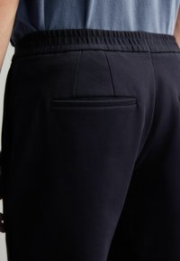 Mørkeblå joggere med elastisk talje, der har en enkelt baglomme og et struktureret stof for en behagelig pasform.