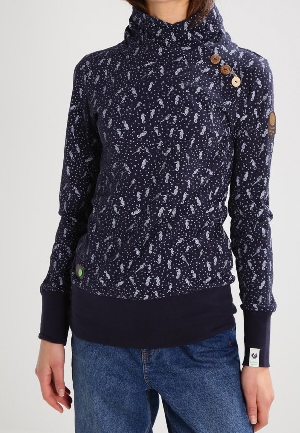 Mörkblå långärmad topp med hög krage, träknappar på axeln, vitt sjöhästmönster, bärs med blå jeans.