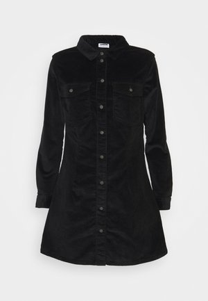 Schwarzes Cordhemdkleid mit langen Ärmeln, spitzem Kragen, Knopfschluss und zwei Brusttaschen. Glatte Textur, Saum bis zur Oberschenkelhöhe.