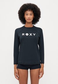 Melna garumām piedurknēm rēvēšanas jaka ar "ROXY" logo baltā krāsā, izgatavota no gludas, elastīgas auduma. Iespējamas raglāna piedurknes un plakano šuvju detaļas.