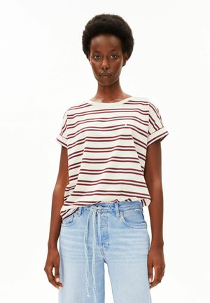 Femme aux cheveux courts bouclés portant un t-shirt à manches courtes blanc et rouge rayé et un jean bleu clair avec un cordon.