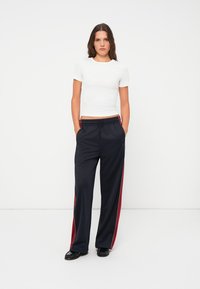 Zwarte joggingsbroek met rode zijstrepen, elastische tailleband en relaxte pasvorm, gecombineerd met een aansluitend wit T-shirt. Glad textuur, casual ontwerp.