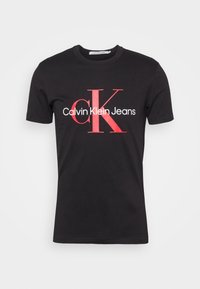 Svart bomullströja med rundad halsringning, prydd med röd "CK" och texten "Calvin Klein Jeans" i en djärv grafisk design. Kortsleeve, vanlig passform.