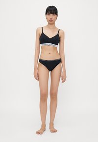 Black lingerie set featuring a bralette with a white logo band and matching low-rise panties, both with a smooth texture and fitted design.