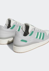 Nízké tenisky Adidas v bílé a šedé barvě s zelenými pruhy a akcenty, které mají polstrované límce a strukturované bílé mezipodešve.