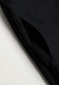 Tissu noir plié montrant une poche fendue soigneusement cousue sur une surface textile lisse et mate.