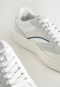 Sneaker bianchi e grigi con tomaia in pelle liscia, dettagli in suede, particolari blu a contrasto e suole in gomma texturizzata.