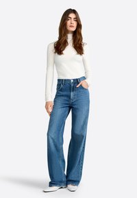 Blue high-waisted wide-leg jeans with a button closure, paired with a fitted white turtleneck. Smooth texture, minimal stitching details.