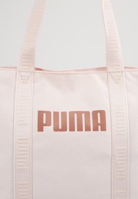 Sac fourre-tout en tissu rose avec un grand logo "PUMA" audacieux en rose doré. Dispose de anses assorties avec un marquage en relief tout au long.