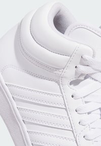 Bijela tenisica s glatkim sintetičkim gornjim dijelom, s podstavljenim ovratnikom, ravnim vezicama i horizontalnim prugama na bočnoj strani.