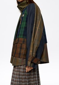 Večbarvna karirana jakna z zelenimi, mornarsko modrimi in rjavimi odtenki, visoko ovratnico in zadrgo. Tekstilirana tkanina z velikimi žepi.