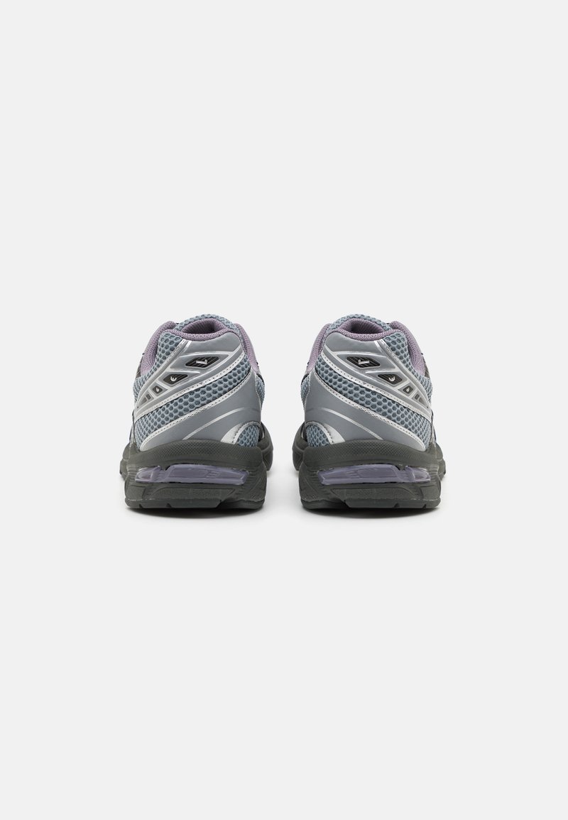 Grijze sportschoenen met meshpanelen, paarse accenten en zwarte rubberen zolen. Reflecterende details lopen langs de zijkanten. Achteraanzicht getoond.