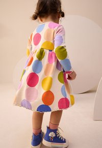 Robe à pois multicolores avec manches longues, comprenant des tons de rose, jaune, vert et bleu, et un ourlet festonné. Baskets bleues avec un motif de nuage.