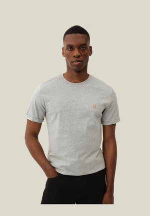 T-shirt grigio in cotone con maniche corte, scollo rotondo e piccolo logo arancione sul lato sinistro del petto, indossato con pantaloni neri.