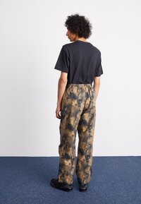 Black short-sleeve t-shirt paired with loose, brown and black tie-dye patterned pants, featuring an elastic waistband and black footwear.