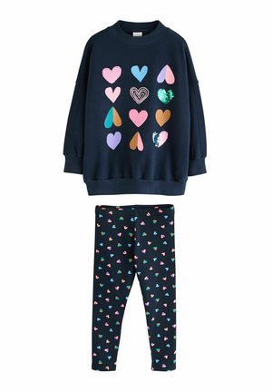 Marineblå sweatshirt med farverige hjerteformer, kombineret med matchende leggings dækket af et flerfarvet hjerte mønster.