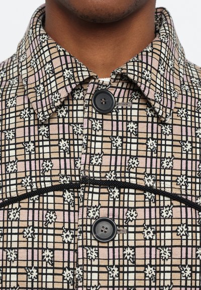Patterned shirt jacket in woven fabric, featuring a grid pattern with pink, beige, and black sections, a collar, and a black button detail.