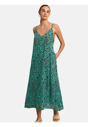 Vrouw die een teal en zwart zebraprint mouwloze maxijurk draagt met spaghettibandjes en beige geweven instapsandalen.