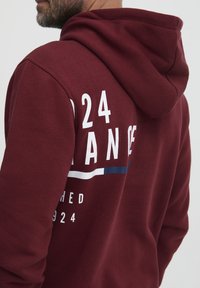 Felpa cappuccio color granata con una grande grafica bianca con il testo "24" e "FRANCE", strisce orizzontali blu e bianche, realizzata in morbido materiale misto cotone.