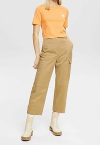 Orange bomullströja med en liten hjärtgrafik, i kombination med beige vida cargobyxor med framfickor och krämfärgade ankelstövlar.