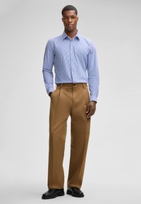 Camicia a maniche lunghe a righe blu chiaro abbinata a pantaloni larghi beige e scarpe nere. Tessuto liscio con bottone sulla vita dei pantaloni.