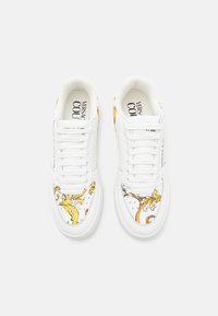 Weiße Sneakers mit dekorativen gelben und schwarzen Mustern an den Seiten, mit Schnürsenkeln, runder Zehenpartie und gepolsterem Innenfutter.