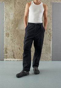 Svarta cargobyxor med ett bälte, som har en lös passform och flera fickor, tillsammans med svarta Crocs. Modellen har på sig en vit t-shirt.