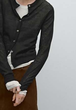 Black, long-sleeve cardigan made of lightweight material, featuring a round neckline and button closure, worn over a white layer.