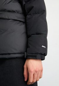 Manga de chaqueta acolchada negra con patrón acolchado, etiqueta de aislamiento 550 y puño ajustable con velcro. Textura suave con acabado mate.