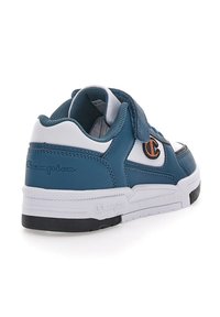 Zapatilla de cuero azul con detalles en blanco, cinta de velcro y forro de malla texturizada. Presenta una suela negra y un logotipo bordado en el talón.