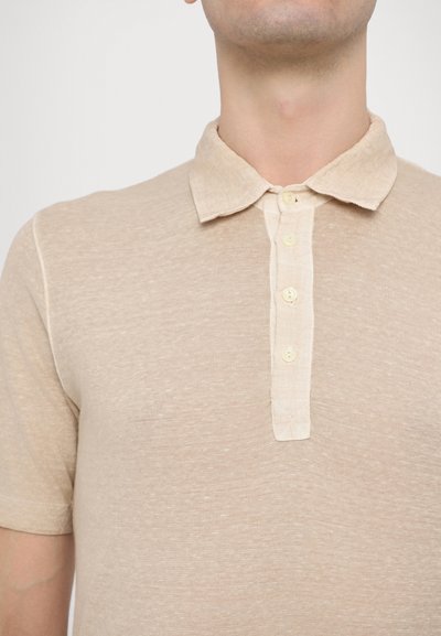 Camisa polo beige hecha de tela texturizada, con un frente de botones que cuenta con cuatro botones crema y un cuello suave y ligeramente alzado.