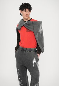 Czerwona i czarna koszula z długim rękawem z logo, zestawiona z szarymi spodniami dresowymi z białymi wzorami graficznymi, materiał miękki i casualowy.