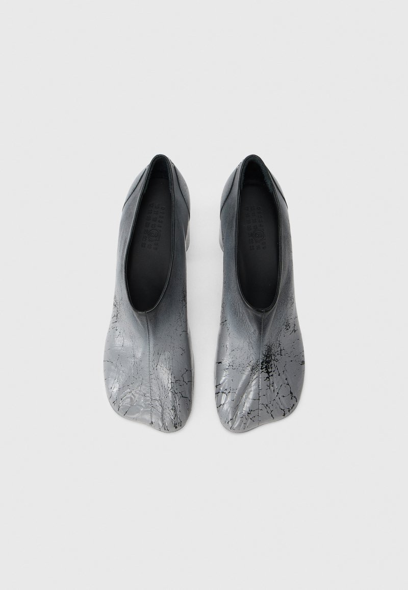 Une paire de chaussures glissantes métalliques argentées avec des détails noirs craqués, un embout carré arrondi et une ouverture basse sur fond blanc.