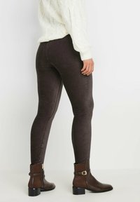 Leggings en velours côtelé marron avec une coupe ajustée, associés à des bottines brunes avec une accent de boucle, et un pull en tricot torsadé blanc.