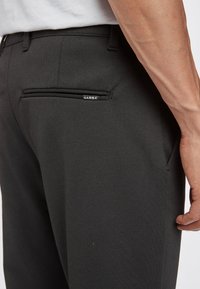 Man i svarta Gabba-byxor med en bakfickan, som visar en del av hans högra arm och hand.