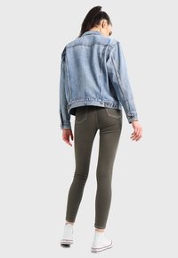 Ljusblå jeansjacka med avslappnad passform, bakfickor synliga. Olivgröna leggings och vita höga sneakers kompletterar outfiten.