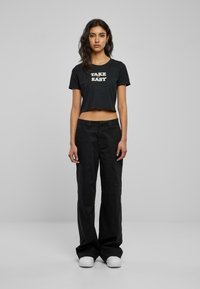 Kuttet svart t-skjorte med teksten "TAKE EASY", kombinert med løse svarte bukser og hvite joggesko. Enkelt design, rund hals og korte ermer.