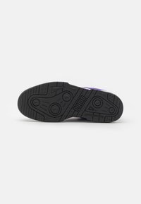 Sort gummisål til sneakers med teksturerede grebmønstre, herunder cirkulære og lineære detaljer. Har et præget brandlogo.