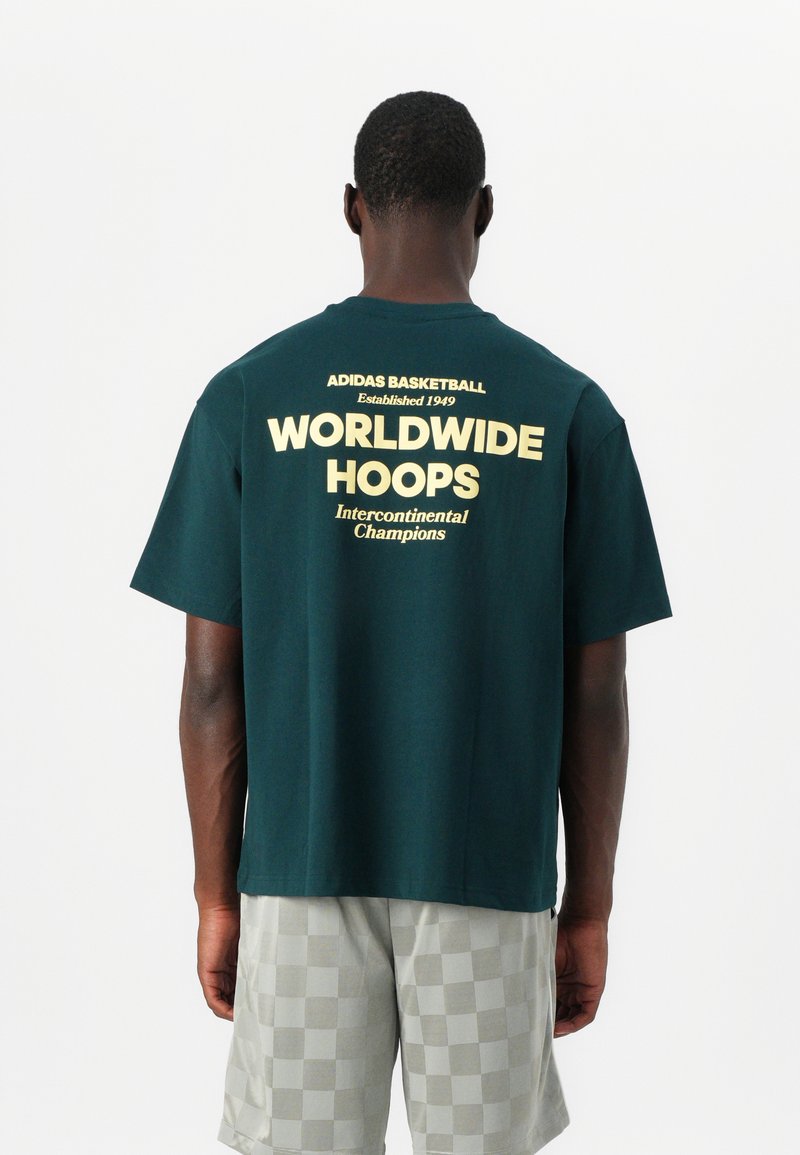 Donkergroen katoenen t-shirt met korte mouwen, met daarachter gele bedrukte tekst: "ADIDAS BASKETBALL," "WORLDWIDE HOOPS," en "Intercontinental Champions."