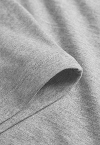 Tessuto di cotone grigio con una texture morbida, che mostra un bordo ripiegato e dettagli di cucitura. La superficie appare leggermente melangiata.
