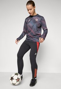Langsleevige, donker bedrukt sporttop met een ronde hals, gecombineerd met zwarte leggings met rode accenten en merklogo's.